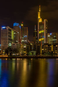 Illuminated buildings by river against sky at night