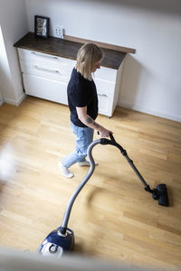 High angle view of young woman using vacuum cleaner on hardwood floor at home