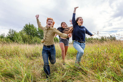 Group of three friends boy and two girls running and having fun together outdoors