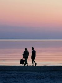 Silhouette people on beach against sky during sunset