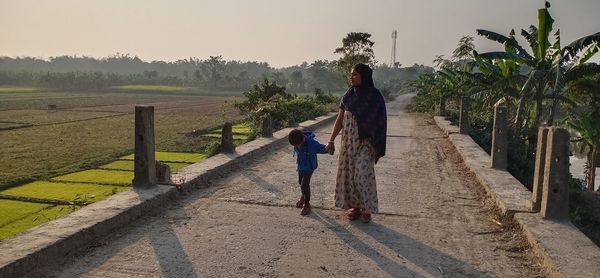 Woman walking with son on road against sky
