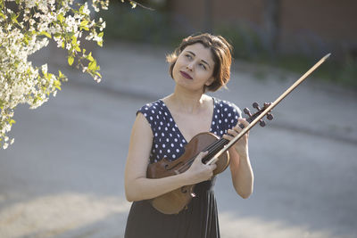 Woman holding violin while standing outdoors