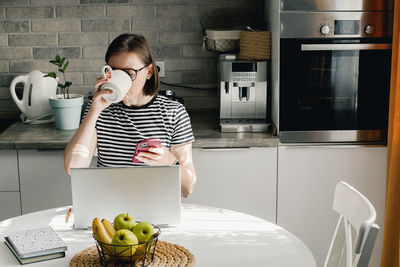 Portrait of young woman using mobile phone while sitting at home