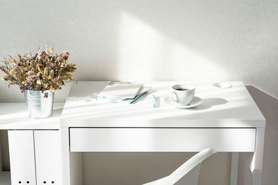 Dried flowers bouquet, coffee cup and stack of books on white table with interesting shadows. 