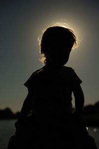 Rear view of silhouette boy standing against sea at sunset