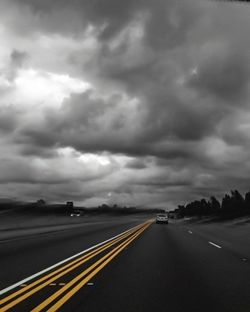 Road leading towards highway against cloudy sky