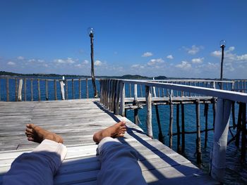 Low section of man relaxing on pier over sea against sky