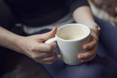 Midsection of person having coffee while sitting on sofa