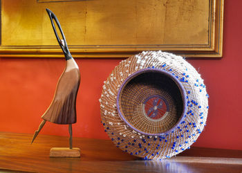 Carved wooden woman figurine standing next to beaded woven basket.