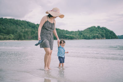 Full length of mother and daughter on beach against sky