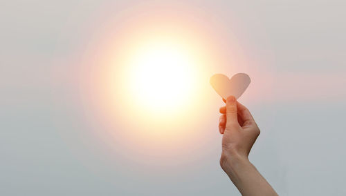 Cropped hand of woman holding ice cream cone against sky during sunset