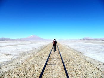 Rear view of man standing on desert against clear blue sky