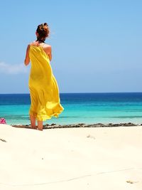 Rear view of woman standing on beach against sky during sunny day