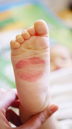 Close-up of person holding baby leg with lipstick kiss 