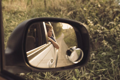 Boy looking away while sitting in car seen through side view mirror
