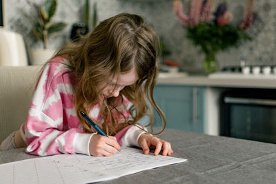 School girl going homework at home, writing in notebook.