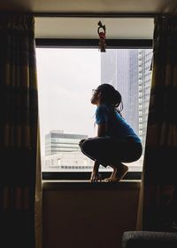 Side view of woman crouching on window sill