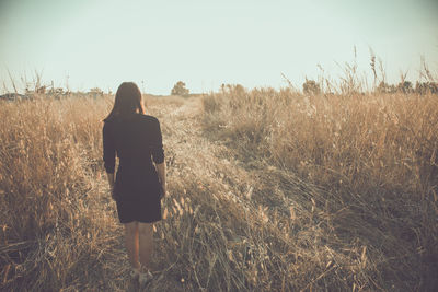 Rear view of woman walking on field against sky