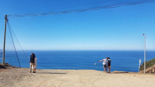 Men standing on beach against clear blue sky