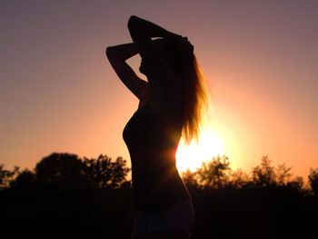 Rear view of silhouette woman standing against orange sky