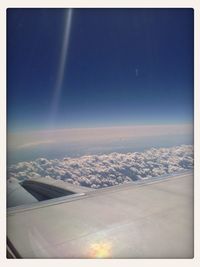 Aerial view of airplane wing over landscape against blue sky