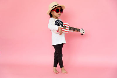 Girl playing guitar against pink background