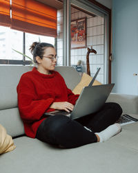 Young woman using laptop while sitting on sofa at home