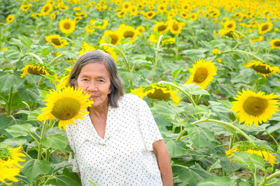 Portrait of smiling woman standing by sunflower