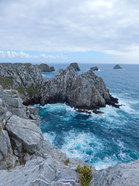 Rock formations in sea against cloudy sky