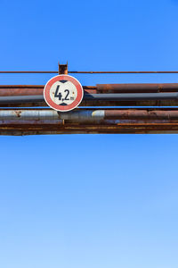 Low angle view of road sign against clear blue sky