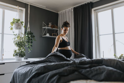 Pregnant woman doing housework and making bed in morning