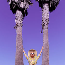 Low angle view of woman by trees against clear blue sky