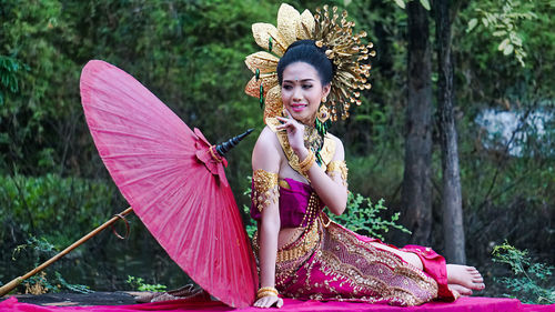 Young woman in traditional clothing with umbrella sitting at forest