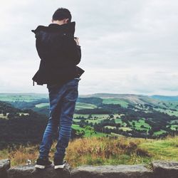 Rear view of boy on phone standing on wall against sky