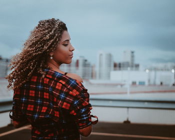 Young woman standing against sky in city