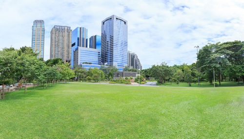 Park by buildings in city against sky