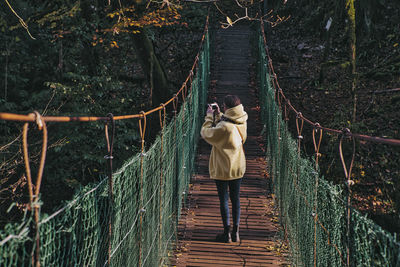 Rear view of man walking on footbridge in forest