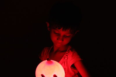 Portrait of boy holding red light against black background