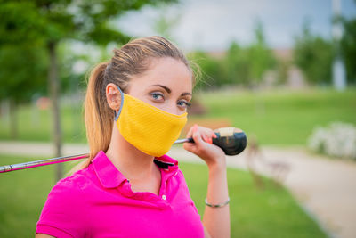 Portrait of woman wearing mask holding golf stick standing in golf course