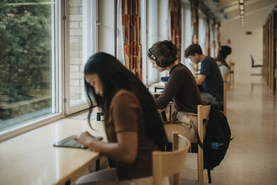 Side view of young woman wearing headphones studying in library at university