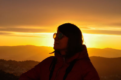 Close-up of young woman wearing sunglasses against orange sky