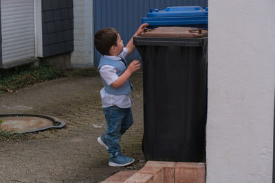 Full length of boy opening garbage bin while standing on footpath