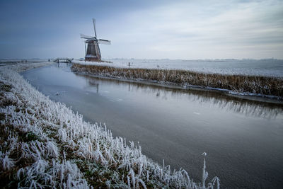 Traditional windmill by sea against sky