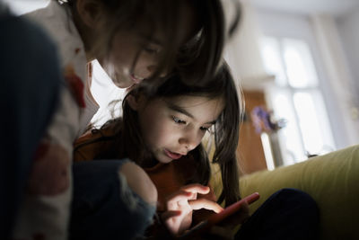 Girl using mobile phone sitting by sister at home