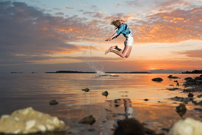 Woman jumping on beach against sky during sunset