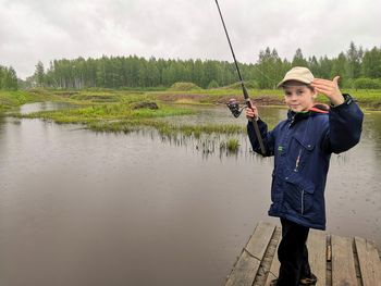 Man holding fishing rod by lake against sky