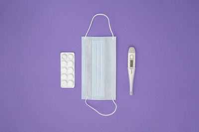 Top view, medical accessories on purple background. mask, thermometer, medicines, pills. flat lay