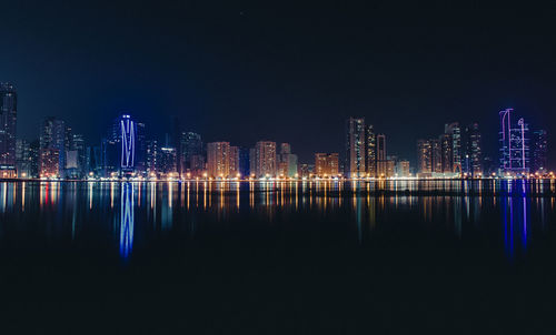 Illuminated city reflecting in river against clear sky at night