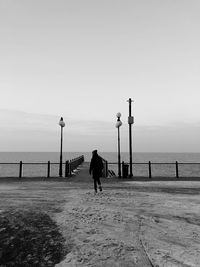 Rear view of woman walking towards sea against clear sky