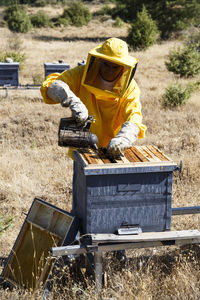 Beekeeper in protective suit using smoker on beehive